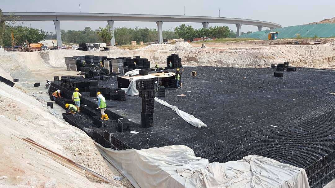 Excavated drainage works lined with geotextile, with modular drainage cells being laid and a rail viaduct behind